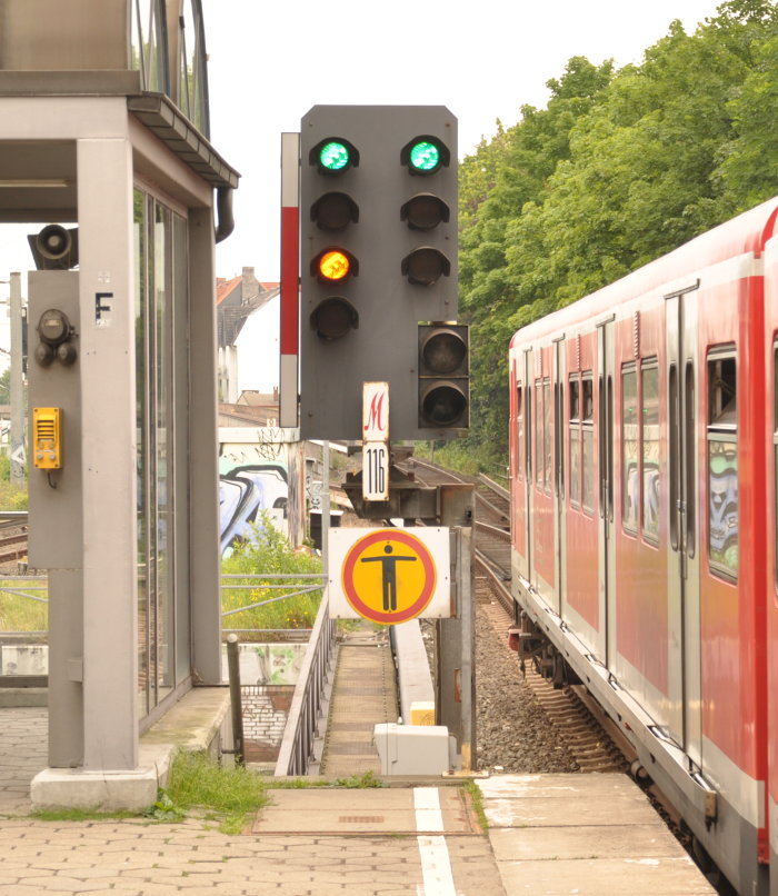 Signal 116 zeigt Sv 4, zwei grüne Lichter waggerecht nebeneinander, unter dem linken noch ein gelbes Licht, rechts daneben der ausfahrende Zug