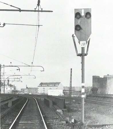 Graustufenfoto des Sv-Signals 201 mit dritter Laterne unten links, es steht rechts vom S-Bahngleis nach Barmbek, über den S-Bahngleisen die Oberleitung, rechts das Gütergleis der Güter-Umgehungsbahn