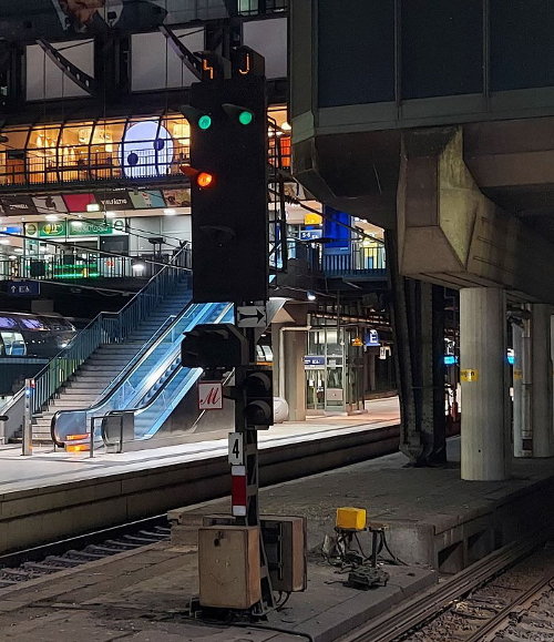 Signal 4 in der nächtlichen Halle des Hbf etwa aus Lokführerperspektive eines vor dem Signal ahltenden Zuges, es zeigt Sv 4, zwei grüne Lichter waggerecht nebeneinander, unter dem linken noch ein gelbes Licht, darüber leuchten der Gleiswechsel- und der Richtungsanzeiger J