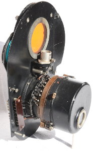 Seitenansicht des Blendenrelais, links oben die Linse, rechts die Glühlampe, links unten das Gegengewicht des Farbscheibenpendels, rechts unten der Antrieb